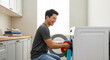 © Iryna - Man loading washing machine and laughing, cleaning chores and home appliance use in modern laundry room
