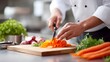 © pkproject - A skilled chef wearing a white uniform precisely slices vibrant orange carrots on a wooden cutting board surrounded by fresh ingredients in a bright professional kitchen setting