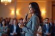 © miss irine - Indian woman in formal suit gives speech at conference. Smiling speaker with microphone addresses audience. Businesswoman giving presentation indoors at a seminar or workshop event.