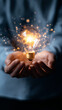 © Curioso.Photography - A glowing light bulb is held gently in a person's hands with sparks around it.