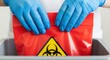 © Tatiana - Woman in blue glove handles red biohazard bag. Medical waste disposal for laboratory safety and infectious materials handling.