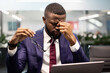 © Prostock-studio - Closeup of exhausted black man manager or businessman sitting at workdesk in front of laptop at modern office, holding glasses and rubbing nose bridge, having headache, burnout at work concept