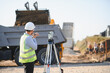 © Serhii - Engineer surveying construction site with dump truck operating