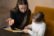 © Volha - Mother patiently explaining concepts to her young daughter while studying a book together at home, creating a supportive learning environment focusing on education and family bonding