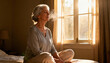 © Anna - Senior woman practicing deep breathing meditation in a sunlit bedroom. Mature person relaxing with a mindfulness exercise in the morning. Healthy lifestyle and well-being concept