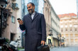 © Jelena - Smiling bearded businessman checking smartphone walking urban street