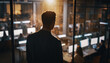© Soleh - Ambitious businessman standing behind a glass wall, observing his dedicated employees working late. A cinematic shot of corporate success and leadership vision