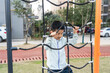 © tai - A young boy is engaged in climbing a rope net in an outdoor playground, showing his active play behavior.