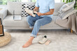 © Pixel-Shot - Man with flat feet inserting orthopedic insole into sneaker on sofa at home