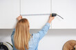 © Pixel-Shot - Mature woman measuring cupboard in kitchen, back view