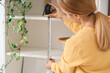 © Pixel-Shot - Mature woman measuring shelf at home, back view