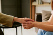 © AnnaStills - Middle aged Caucasian woman holding hand of young adult Caucasian woman offering support during psychological counseling session in office setting, hands visible in close up