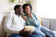 © Daniel - Happy couple sharing bowl of popcorn watching tv on sofa at home