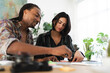 © Studio Marmellata - A diverse man and woman collaborate at a bright table, reviewing documents and notes. They are engaged in a productive discussion in a modern, plant-filled office or home.