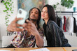 © Studio Marmellata - A young man with dreadlocks holds a smartphone to take a selfie with a smiling young woman. They are a diverse pair capturing a happy moment indoors.