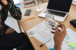 © Studio Marmellata - A person holds an instant photo of two friends, reminiscing about travel memories. Maps, a laptop, and a printer are on the table, suggesting trip planning.