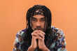 © Studio Marmellata - A young Black man with dreadlocks and a patterned headband gazes intently at the camera. His hands are clasped under his chin, showing a contemplative expression. He wears a colorful shirt.