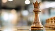 © Sergey - close up of a single wooden king chess piece standing on a board, blurred office interior in background, strategic concept, beautifully carved glossy