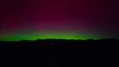 © AmazingAerialAgency - Aerial view of a vibrant aurora borealis paints the night sky with strokes of green and magenta over the dark silhouette of distant mountains, Fruita, Colorado, United States.