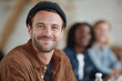 © SolaruS - Confident, friendly man smiles at camera. Diverse group blurred in background. Represents leadership, teamwork, creativity,  community. Use for business, education.