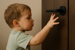 © Aleksandra - Curious toddler reaching for black door handle, innocent child exploring environment, safety risk at home, learning through touch