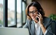 © guo - Happy smiling mature middle aged business woman, busy professional hr or bank manager talking on the phone making business call on cellphone at work in office using laptop. High quality