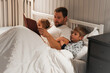 © Marina Demidiuk - Happy mature 40 year old father reading book to his curious children lying in a bed before the sleep. Dad, little daughter and son spending time together. Family read the fairy story. Evening bedroom.