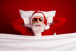 © deagreez - Cheerful Santa Claus lying in bed with sunglass smiling on a festive red background, spreading holiday cheer and joy