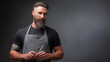 © Tetyana - Professional male barber with a stylish beard and modern haircut wearing a grey apron, holding a straight razor, and observing the camera on a dark background