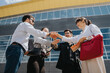 © qunica.com - A group of business colleagues engaged in conversation, standing outside near a modern office building, sharing a handshake gesture showcasing unity and collaboration.