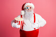 © deagreez - Santa in red suit with popcorn bucket and 3D glasses poses against pink background for festive christmas promotion