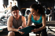 © Home-stock - Man and woman engaged in fitness discussion in gym, reviewing plan of training, likely focusing on workout or nutrition plan