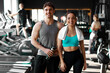 © Home-stock - Happy European couple after workout, man with water bottle and woman with towel on her shoulders posing in gym and smiling at camera