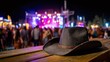© Ірина Пальцева - Western vibes at the festival! A cowboy hat sits on a wooden table, the crowd blurred in the background enjoying the music and lights. A night to remember. Yeehaw!