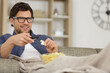 © auremar - smiling-man sitting on sofa watching tv and eating chips