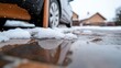 © Valentyna - Melted snow lies on a wet, brown surface near a parked car, reflecting the scene in a puddle
