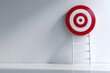 © Vitaliy - A red and white target stands prominently on a ladder against a plain wall, symbolizing ambition and the journey toward success and achievement in life