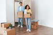 © Prostock-studio - A young couple carries boxes into their new home, smiling and looking excited. The spacious room is mostly empty and has wooden floors, creating a warm, welcoming atmosphere.