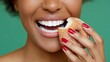 © Nataliia_Trushchenko - A woman is eating a doughnut with sugar on it. She has red nails and a smile on her face