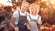 © Prostock-studio - A happy couple stands in their garden surrounded by fall colors, holding gardening tools. They smile while showcasing pumpkins and flowers, enjoying the beauty of autumn.