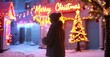 © antishock - Person views festive holiday lights. Snowy scene evokes winter warmth, joy, celebration. Bright colors illuminate building facade.