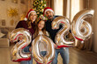 © Home-stock - Overjoyed family celebrating Christmas at home, having fun holding giant balloons shaped as numbers 2026
