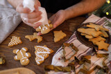 Man making gingerbread christmas cookies. Hands decorating cookies with icing on table with fir branches and lights, atmospheric eve. Winter holiday preparation