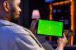 © DC Studio - Young male freelancer uses green screen mockup on modern tablet to work in the living room, sitting at home with the gadget and solving tasks. Relaxed casual young adult in his trendy space.