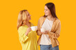 © Pixel-Shot - Pretty young woman with her mother and cups of tea on yellow background