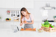 © Look Aod 27 - Attractive woman is using a digital tablet to follow a recipe while actively preparing fresh ingredient in like carrot and holding capsicum in a bright modern white kitchen.