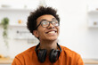 © Sofiia Shunkina - A young Black man with glasses smiles while looking up, with headphones around his neck.