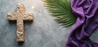 © miss irine - Stone cross, fresh green palm leaf, flowing purple cloth rest on textured grey background. Spiritual arrangement faith, devotion, solemn remembrance for Christian observances like Lent, Easter.