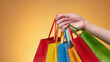 © Luce - Close-up of a hand holding bright colorful shopping bags with textured handles against a vibrant yellow background, representing retail, purchase and seasonal shopping