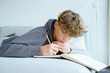 © TrueShot | Westend61 - Boy lying on sofa writing in notebook at home
